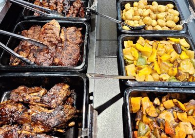 Hot trays of cooked kosher meats, roasted potatoes and vegetables